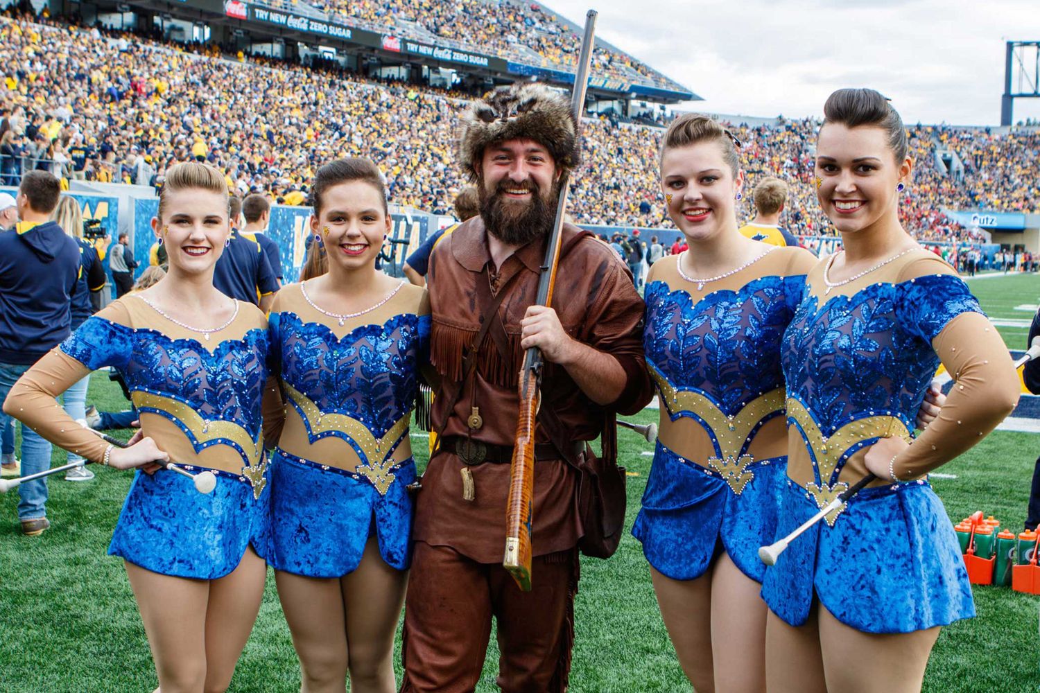 mountaineer stands with twirlers on the football field